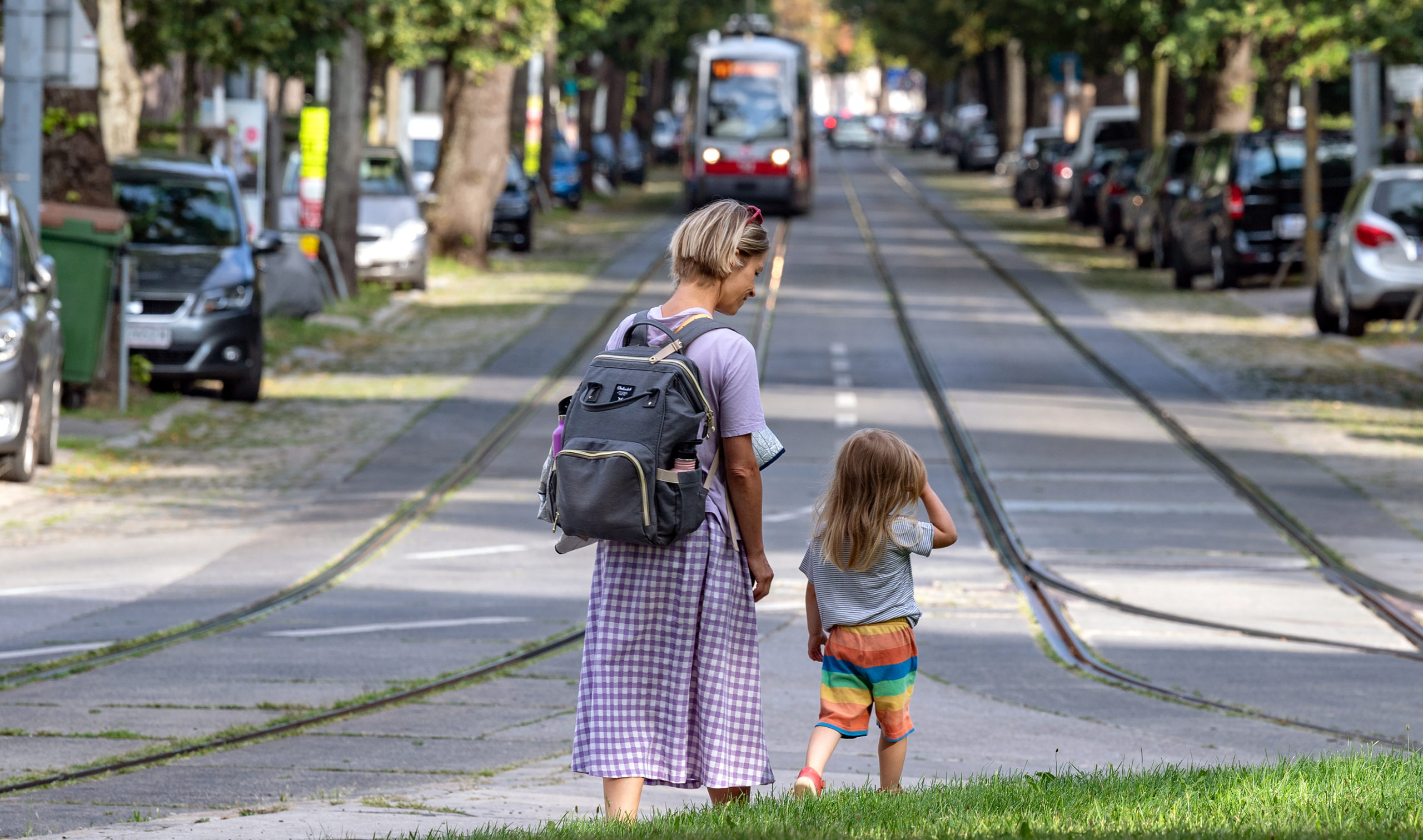 Mutter mit Kind von hinten auf einem Rasenstreifen nahe Straßenbahngleisen in Pötzleinsdorf.