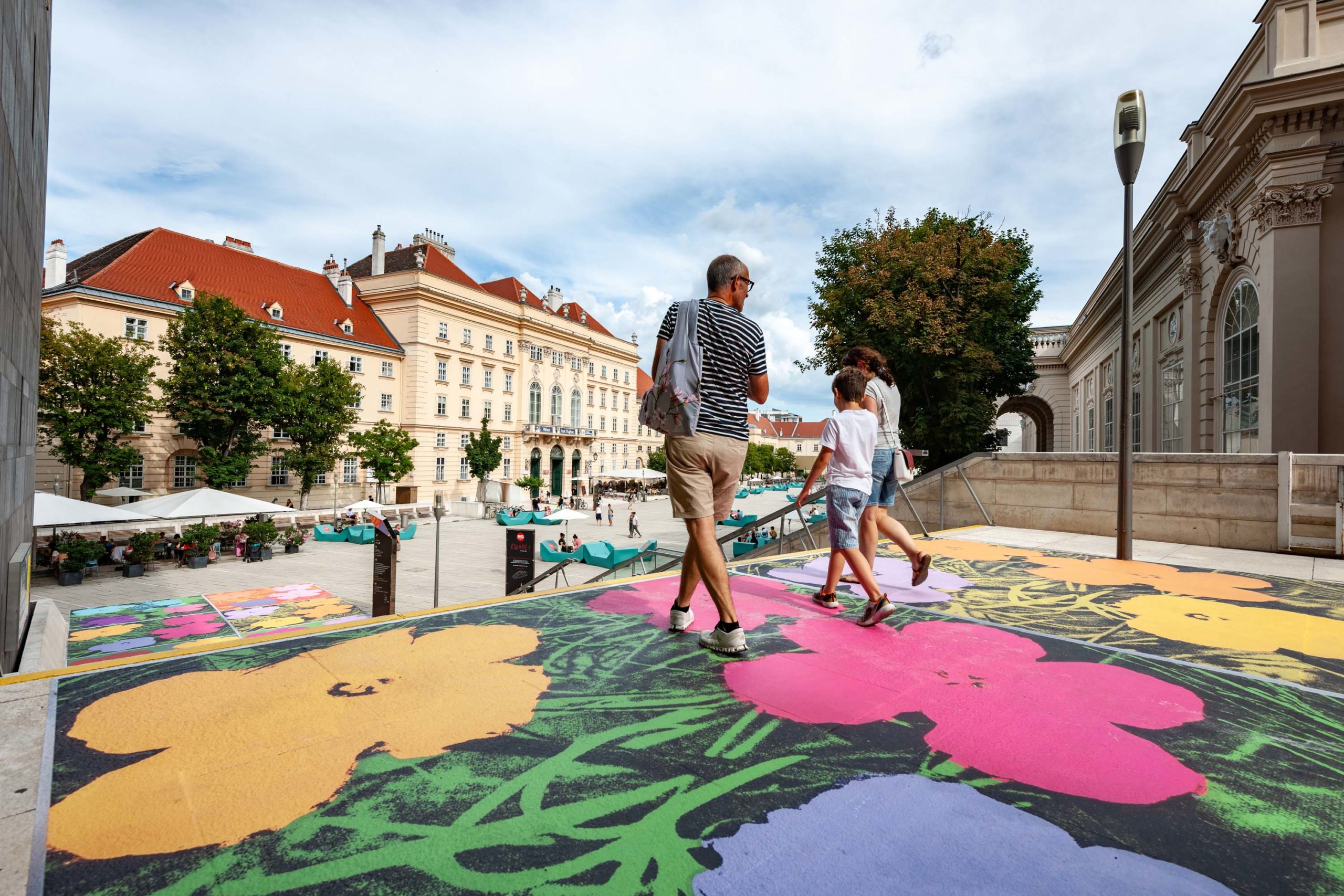 MQ_57 Drei Personen von hinten auf dem Freilufttreppenabsatz im Museumsquartier. Der Asphalt ist mit einem großflächigen Blumenmuster bemalt.© Stadt Wien / Gerd Götzenbrucker