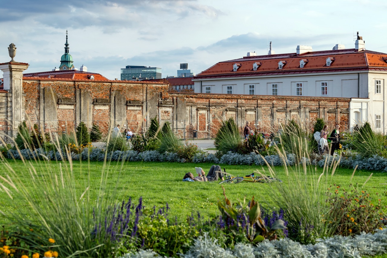 Augarten 2022 Ein Blick in den Augarten. Im Vordergrund eine Liegewiese, auf der ein Mensch ein Buch liest, daneben ein Fahrrad.